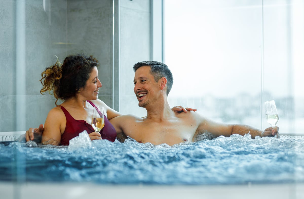 Middle aged couple relaxing in hot tub at spa and drinking champagne